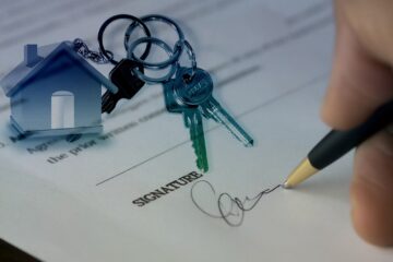 Caneta assinando um contrato e chaves em cima do papel